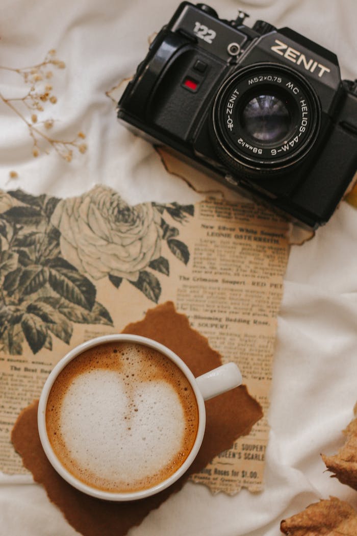 A vintage Zenit camera and latte on a warm fabric setting.